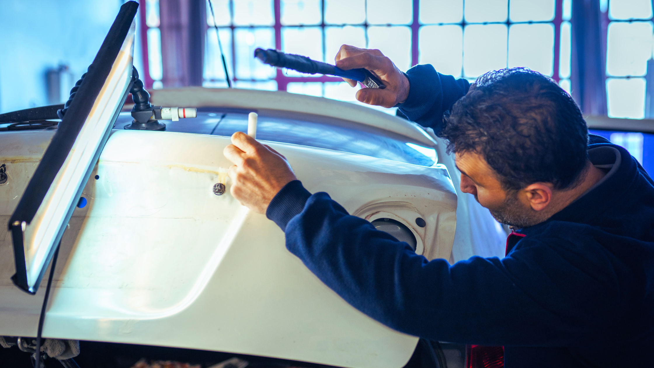male auto body technician performing paintless dent repair with tools